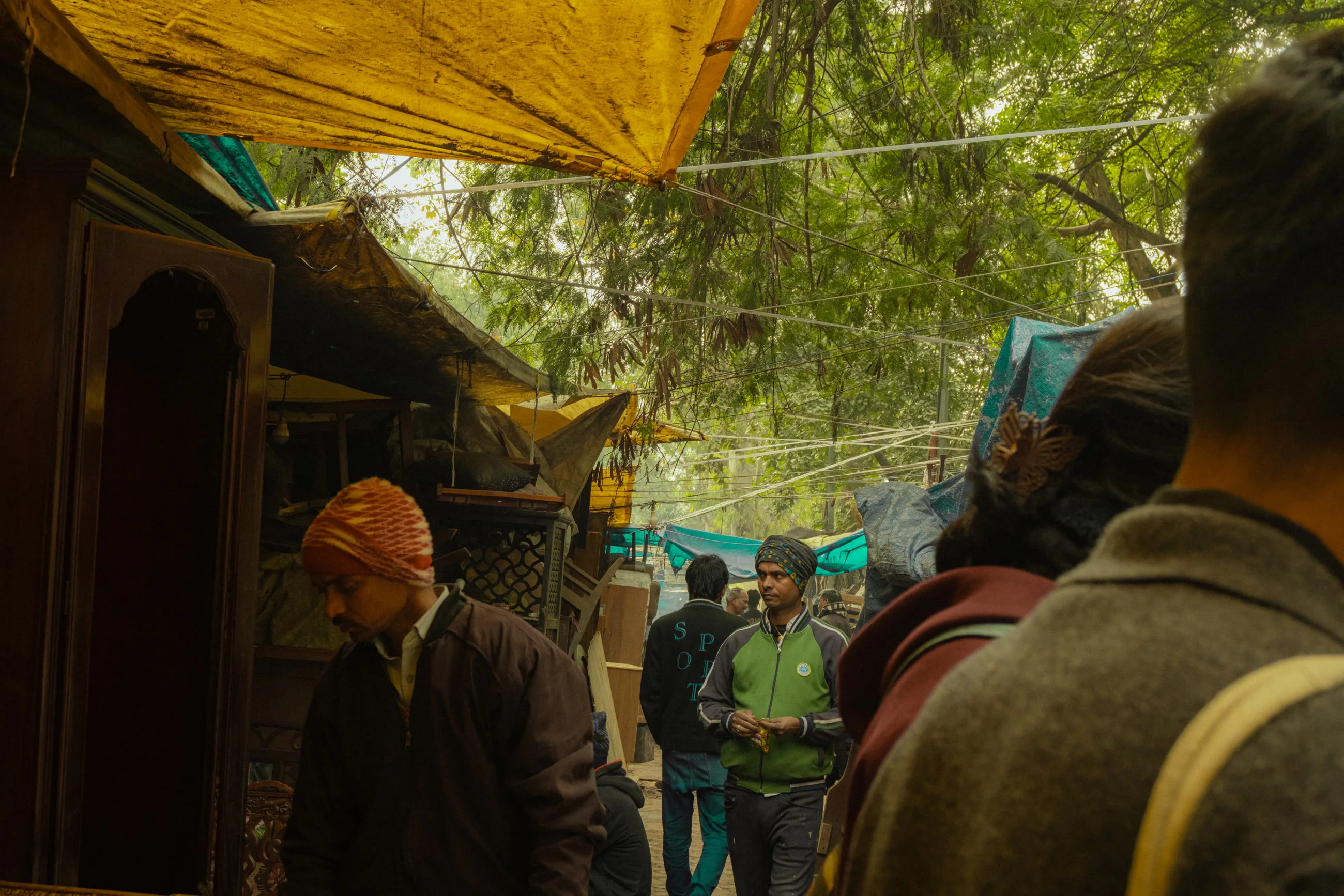 A lane of the market under green netting, dappled with winter light