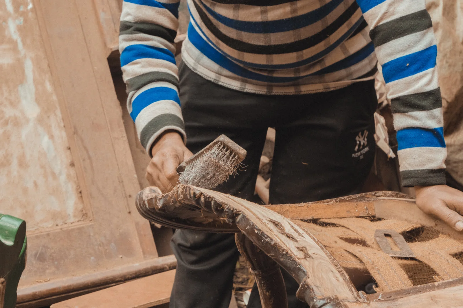 A worker scraping sagwan teak with a makeshift wire brush to mimic age