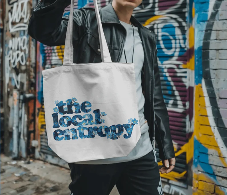 A canvas tote printed with the wordmark, carried against a graffiti wall